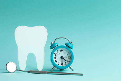 White human tooth figurine on a blue background with a clock and a dental mirror with space for text