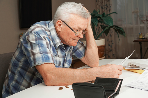Upset depressed Senior man sitting at the table and calculating finances. Old man checking bills. Man counting coins on the table. Pension calculation concept