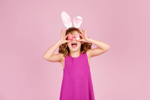istock Delighted child covering eye with eggs during Easter party in pink studio 1369287410