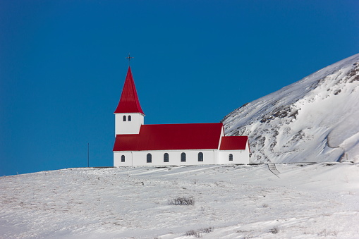Snowy winter landscape with the red colored roof small church (Reyniskirkja) of Vik i Myrdal village located on southern Iceland,