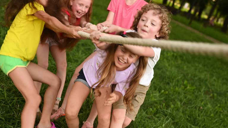 group of preschool children - boys and girls compete in a tug of war against the background of a park and greenery