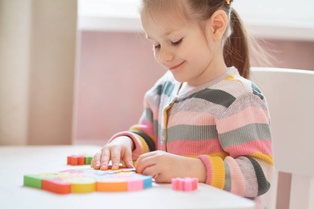 Little girl in colorful sweater plays with wooden puzzle at home. stock photo