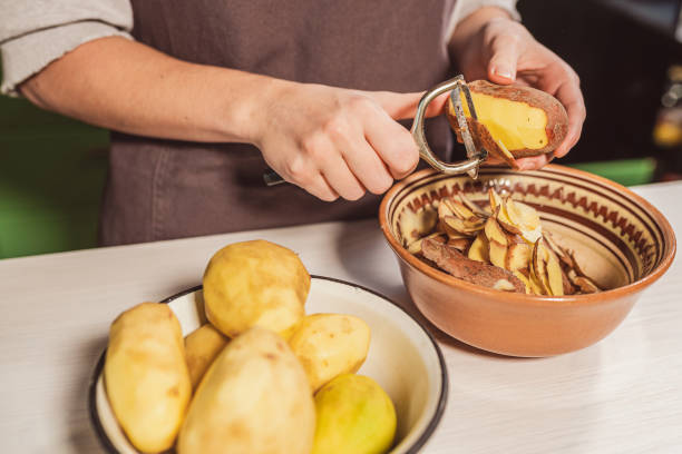 hands of cook with kitchen knife for peeling vegetables cut peel of raw potatoes - potato skin imagens e fotografias de stock