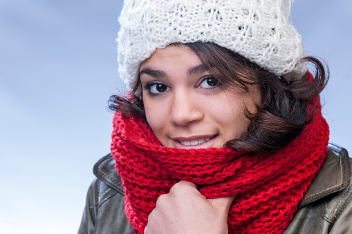 head and shoulders shot of a smiling young woman wearing winter coat, white knit hat and red woollen shawl looking at the camera