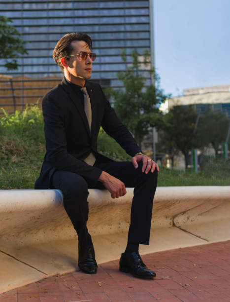 istock handsome man dressed with formal black suit sitting on a bench of a square 1369292968