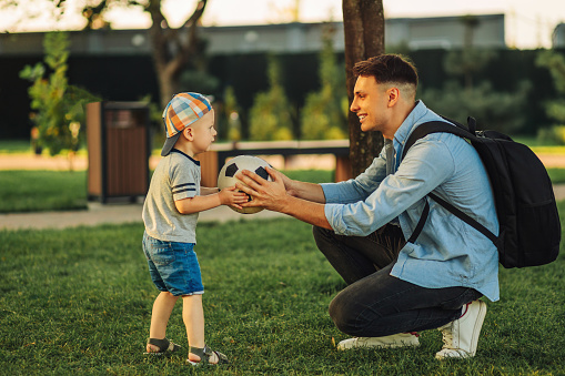 father and son playing together with a soccer ball in the park. Dad with a child play football on a green grassy lawn on a summer day. The concept of outdoor activities, family, Father's Day