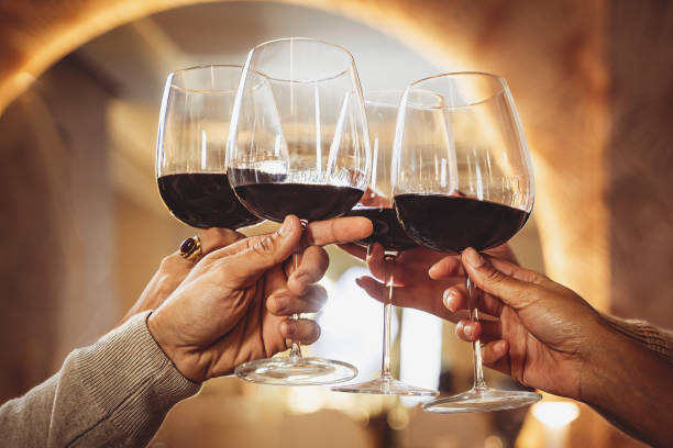 groupe d’amis clignotant des verres à vin avec du vin rouge au restaurant - gros plan se concentre sur les mains tenant des verres et grillant - table on wine alcoholism photos et images de collection