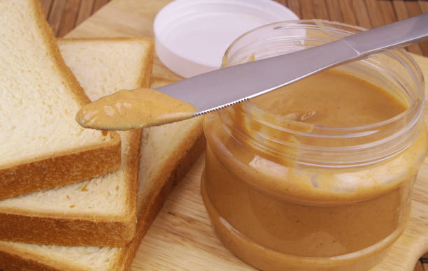 istock Close up of peanut butter spread with bread slices and table knife 1369296463