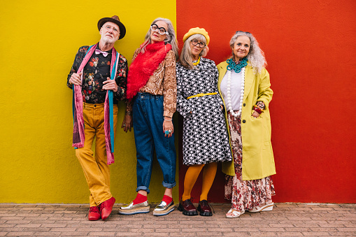 Vibrant senior friends looking at the camera while standing together against a colourful wall. Group of four elderly people feeling confident and youthful in colourful clothing.