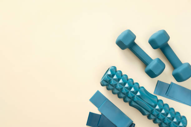 istock Workout equipment for training at home top view. Flat lay blue dumbbells, elastic bands, exercise roller on beige background 1369301470
