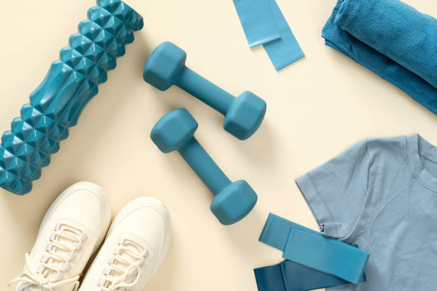 istock Fitness and workout equipment top view. Flat lay dumbbells, exercise roller, elastic bands, feminine sneakers, t-shirt on beige table. 1369301495