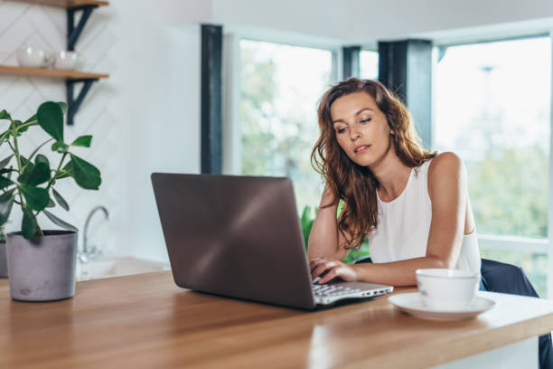 istock Woman is sitting at the kitchen table with laptop 1369302007