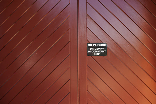 Black metal No Parking sign on a brown wooden garage door.