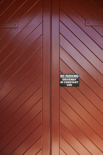 Black metal No Parking sign on a brown wooden garage door.