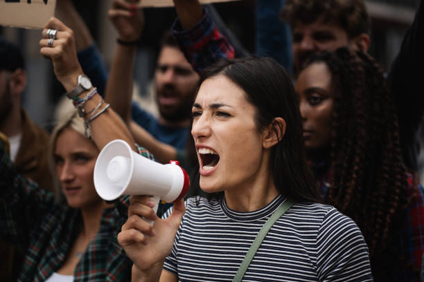 istock Young woman manifesting marching on a protest shouting into a megaphone 1369305281