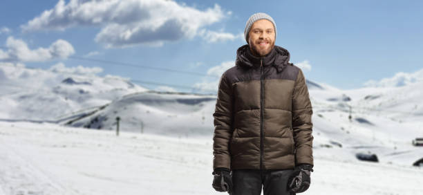 Young man in a winter jacket and pants standing on a snowy mountain