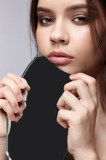 istock Female with mirror shard in hand posing on gray background. 1369307146