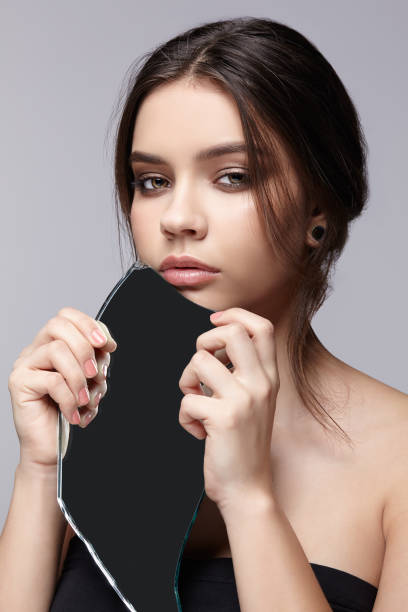 istock Female with mirror shard in hand posing on gray background. 1369307162