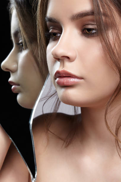 istock Female with mirror shard in hand posing on gray background. Face reflection in mirror splinter. 1369307242