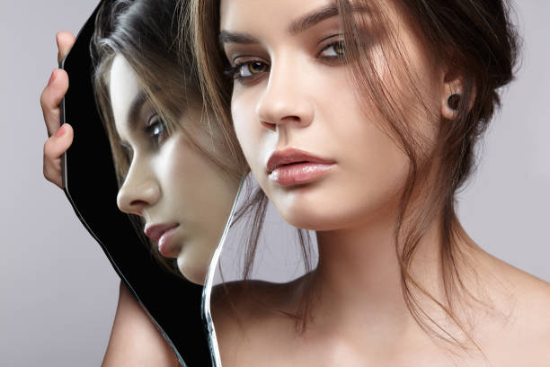 istock Female with mirror shard in hand posing on gray background. Face reflection in mirror splinter. 1369307250