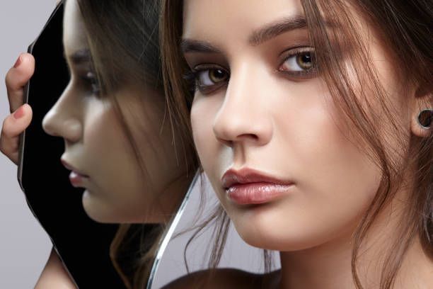 istock Female with mirror shard in hand posing on gray background. Face reflection in mirror splinter. 1369307253