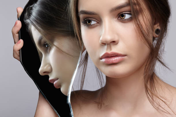 istock Female with mirror shard in hand posing on gray background. Face reflection in mirror splinter. 1369307271
