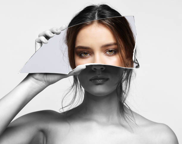 Girl covers her face with a shard of the mirror. Female with mirror shard in hand posing on gray background Black and white portrait of female with mirror shard in hand posing on gray background. Girl covers her face with a shard of the mirror. Eyes reflection in mirror splinter sliver of light on face stock pictures, royalty-free photos & images