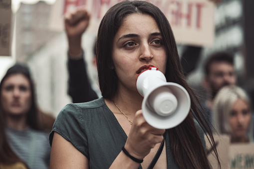 Portrait of a female activist in a protest march holding a megaphone with crows behind her