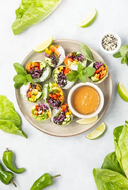 Vegan rainbow-colored spring rolls served with peanut sauce, top down view