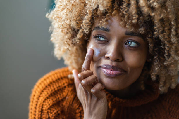 Skin care A close-up of an attractive African-American woman applying face cream to keep it fresh and soft. black skin stock pictures, royalty-free photos & images