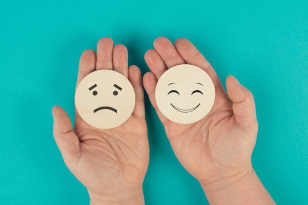 Holding two wooden circles in the hands one face is sad the other one is smiling, porsitive and negative emotions, rating concept, choosing the mood stock photo