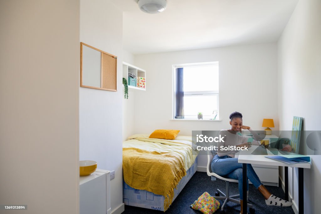 Relaxing in her University Dorm Female student texting on her mobile phone sitting at her desk in her university bedroom in the North East of England. Dorm Room Stock Photo