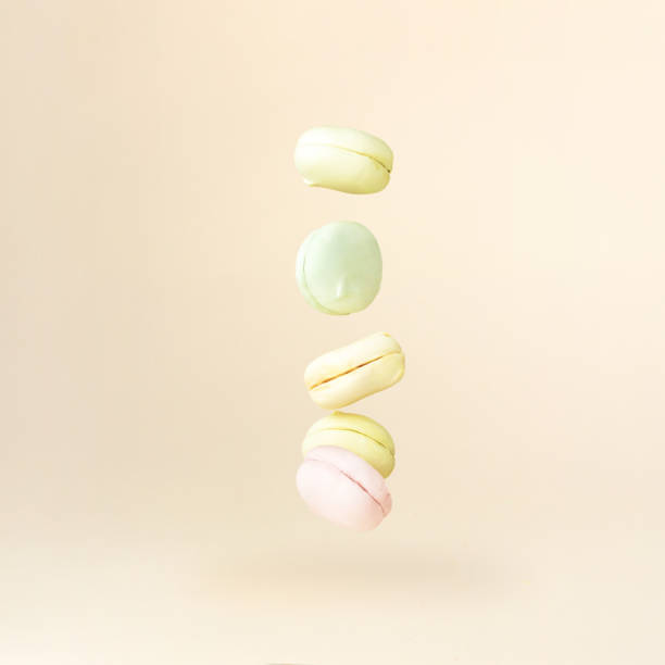 Different types of marshmallows looks like macaroons in motion falling on beige pastel background.