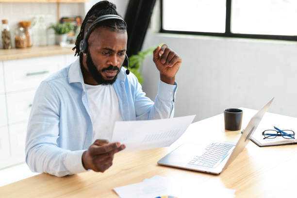 istock African American man in headset working remotely at home using laptop. Employee working online analyzing sales report while sitting at home 1369315842