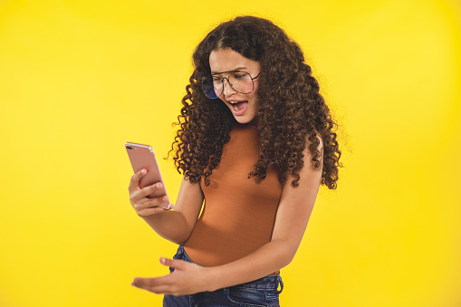 Beautiful teenager on yellow background with her smart phone