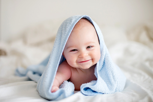 Cute little baby boy, relaxing in bed after bath, smiling happily, daytime