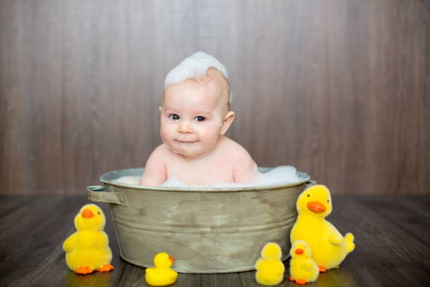 Cute baby playing with rubber duck while sitting in metal basin at home