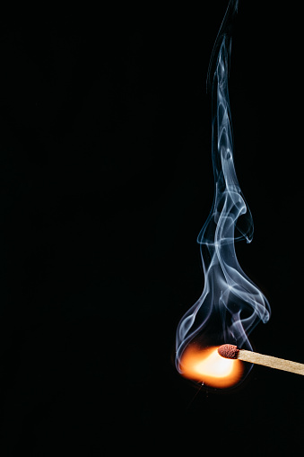 Close up of a lit matchstick in front of a black background
