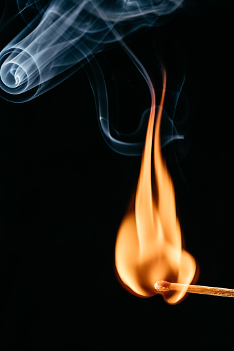 Close up of a lit matchstick in front of a black background