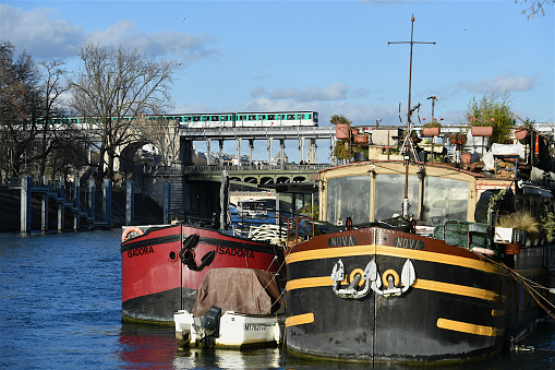 Paris, France-02 05 2022: Subway train passing on the Bir-Hakeim bridge in Paris, France over moored boats on the Seine river.