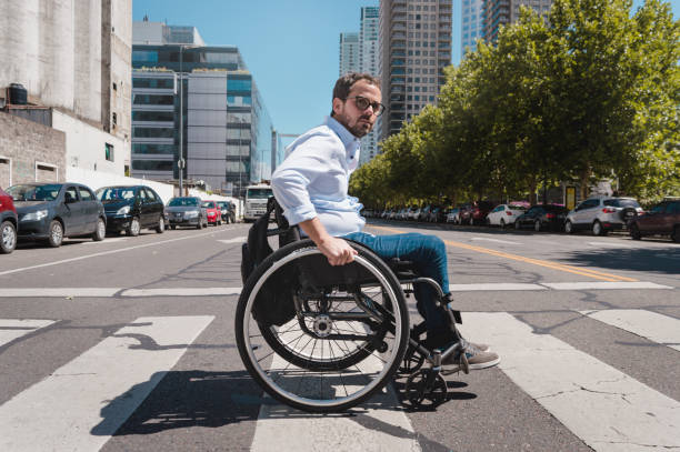 adult man in a wheelchair crossing the street with caution stock photo