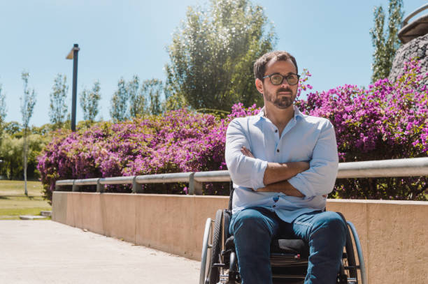 portrait of serious caucasian adult man in a wheelchair in a park stock photo
