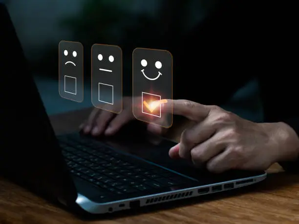Photo of A man uses laptop to select a facial smiling emoticon to display on the virtual screen. A survey, poll, or questionnaire designed to gather information about user experience or customer satisfaction.