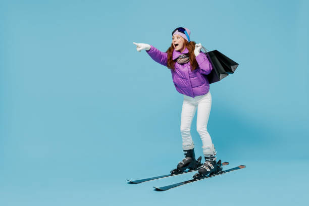 따뜻한 보라색 재킷 스키 고글 마스크에 전신 스키어 여성은 일반 파란색 배경 스튜디오에서 옆으로 분리 쇼핑 포인트 손가락 후 구매와 패키지 가방을 들고 산에서 주말을 보낸다 - ski women winter fashion 뉴스 사진 이미지