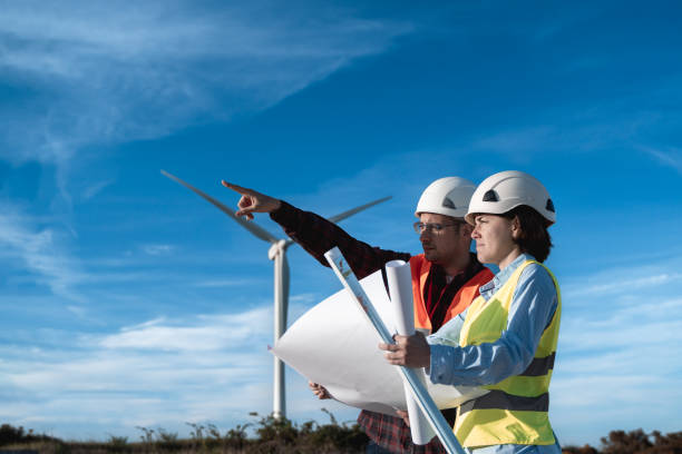 혁신 및 녹색 전력 개념 - 풍력 터빈을 배경으로 대체 에너지를 위해 일하는 사람들 - alternative energy electricity wind turbine team 뉴스 사진 이미지