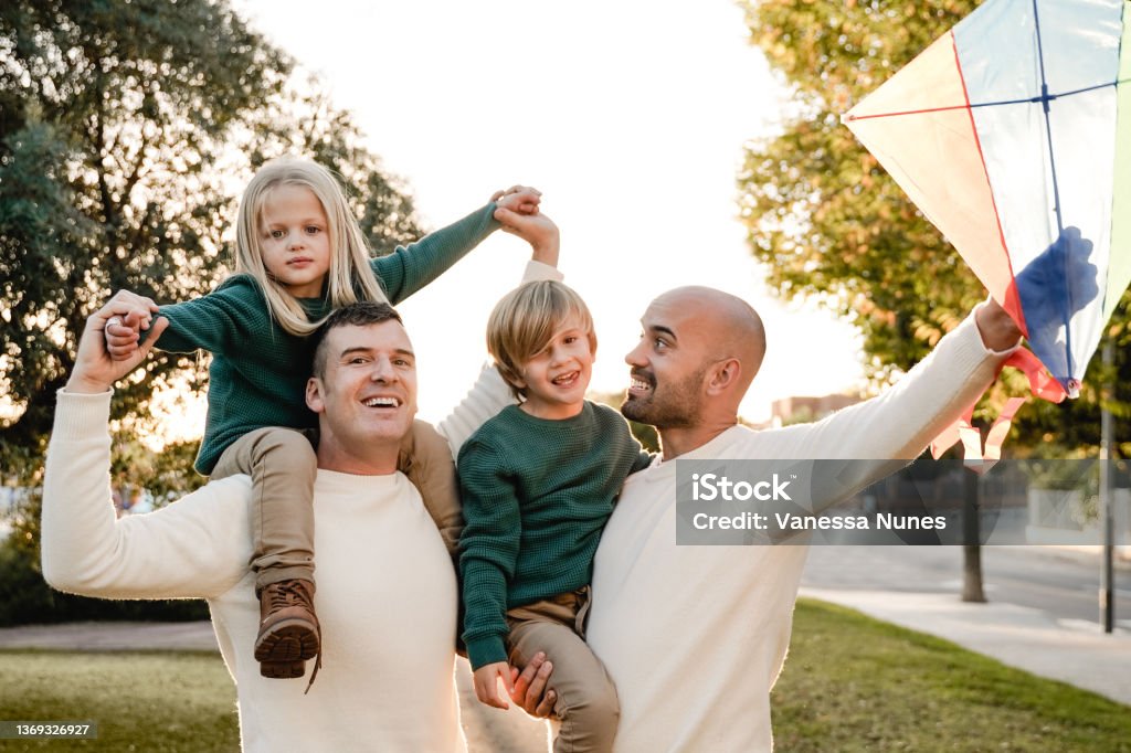 Gay fathers and children playing together at city park - LGBT family love concept - Main focus on left man face Family Stock Photo