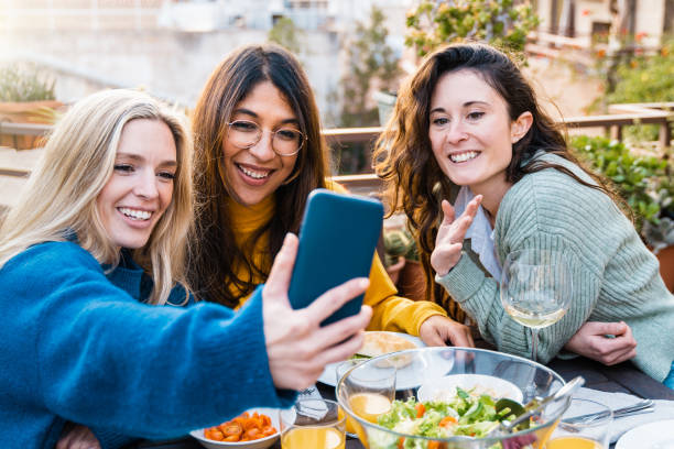 istock Multiracial friends having fun doing video call with mobile phone during vegan dinner at patio restaurant - Focus on African girl face 1369326945