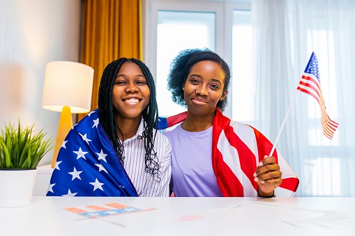 two happy african american sister celebrating usa independence day at home in cozy apartment.