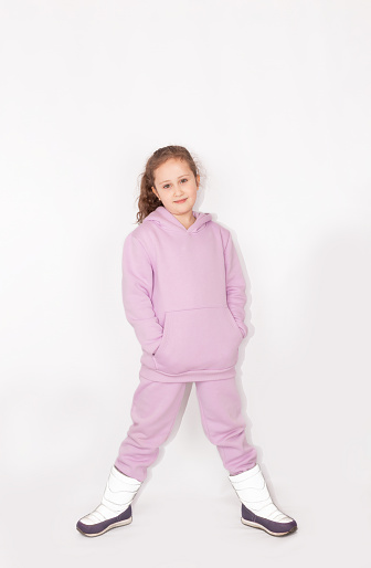A happy little girl in a pink warm suit with a hood, isolate on a white background. Stylish fashionable kid. Stylish trendy kid in hoodie. Full-length photo