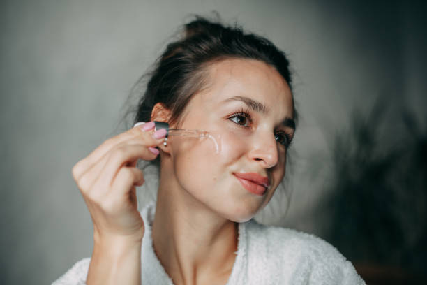 Brunette woman 30 years old applies serum on her face Brunette woman with long hair in a bun 30 years old applies serum on her face at home in the bathroom face serum stock pictures, royalty-free photos & images